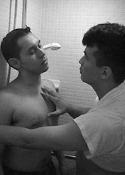 A man is shaving another mans face in the bathroom.